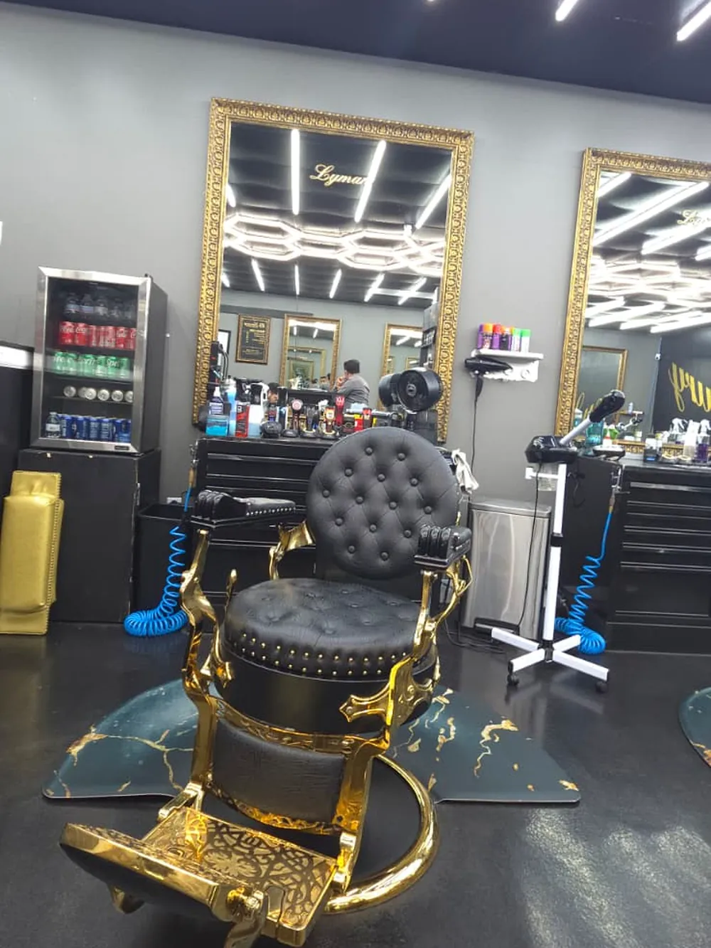 A gilded barber chair on the shop floor, with the drinks fridge and gold-framed mirrors behind it